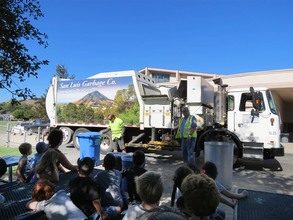 Two San Luis workers with garbage truck speaking to community members and kids.